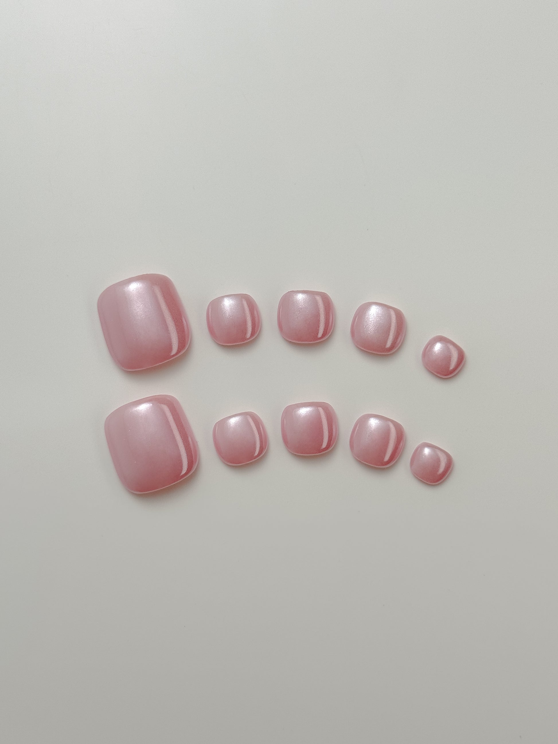 Set of pink glow press-on nails for toes on a light gray background