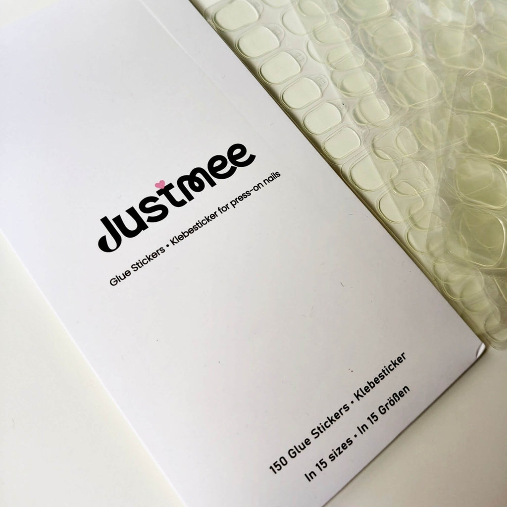 An overview of multiple sheets of transparent double-sided nail adhesive tabs next to their white branded envelope, showing the 150-piece refill set.