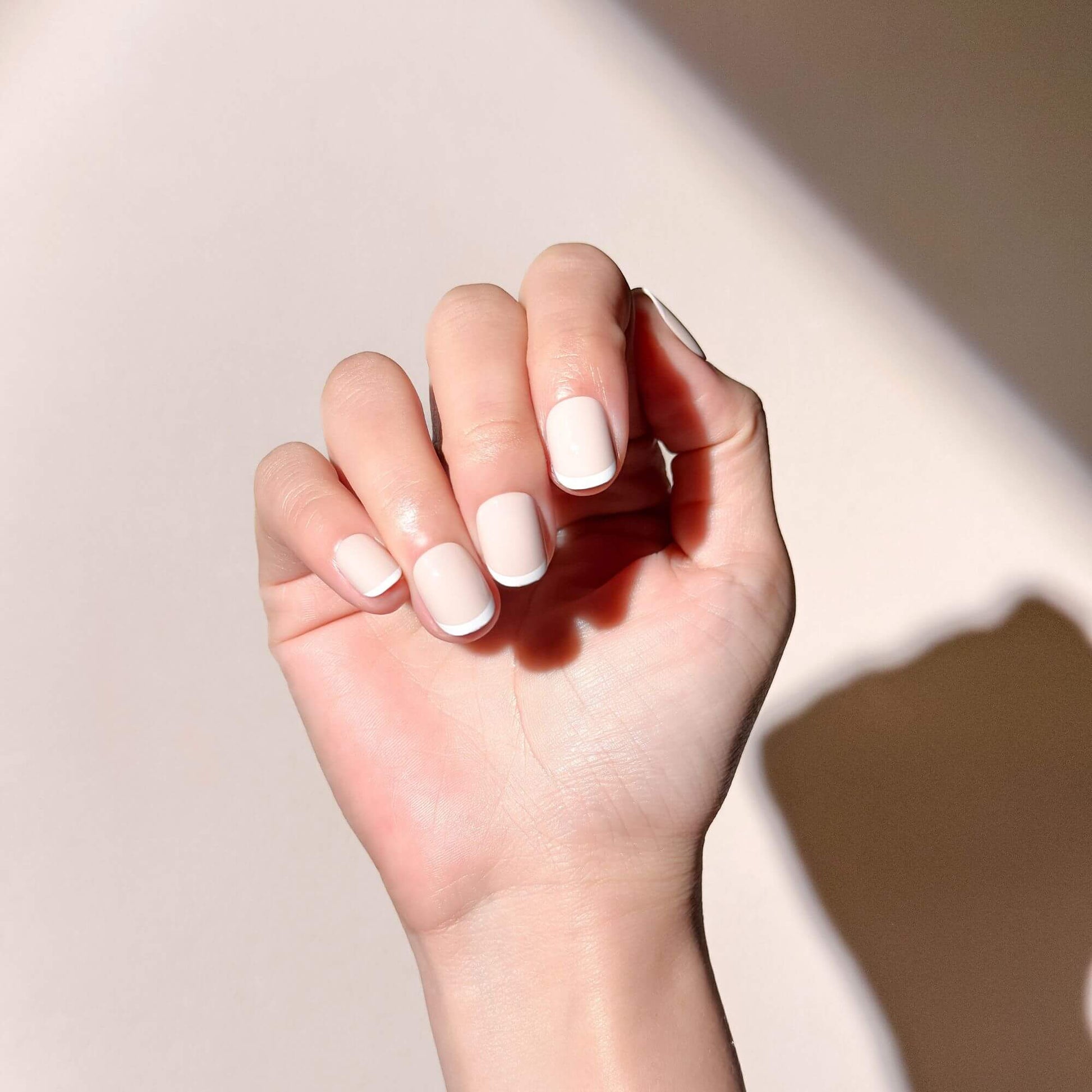 A hand wearing short oval nude nails with a classic white micro french design.