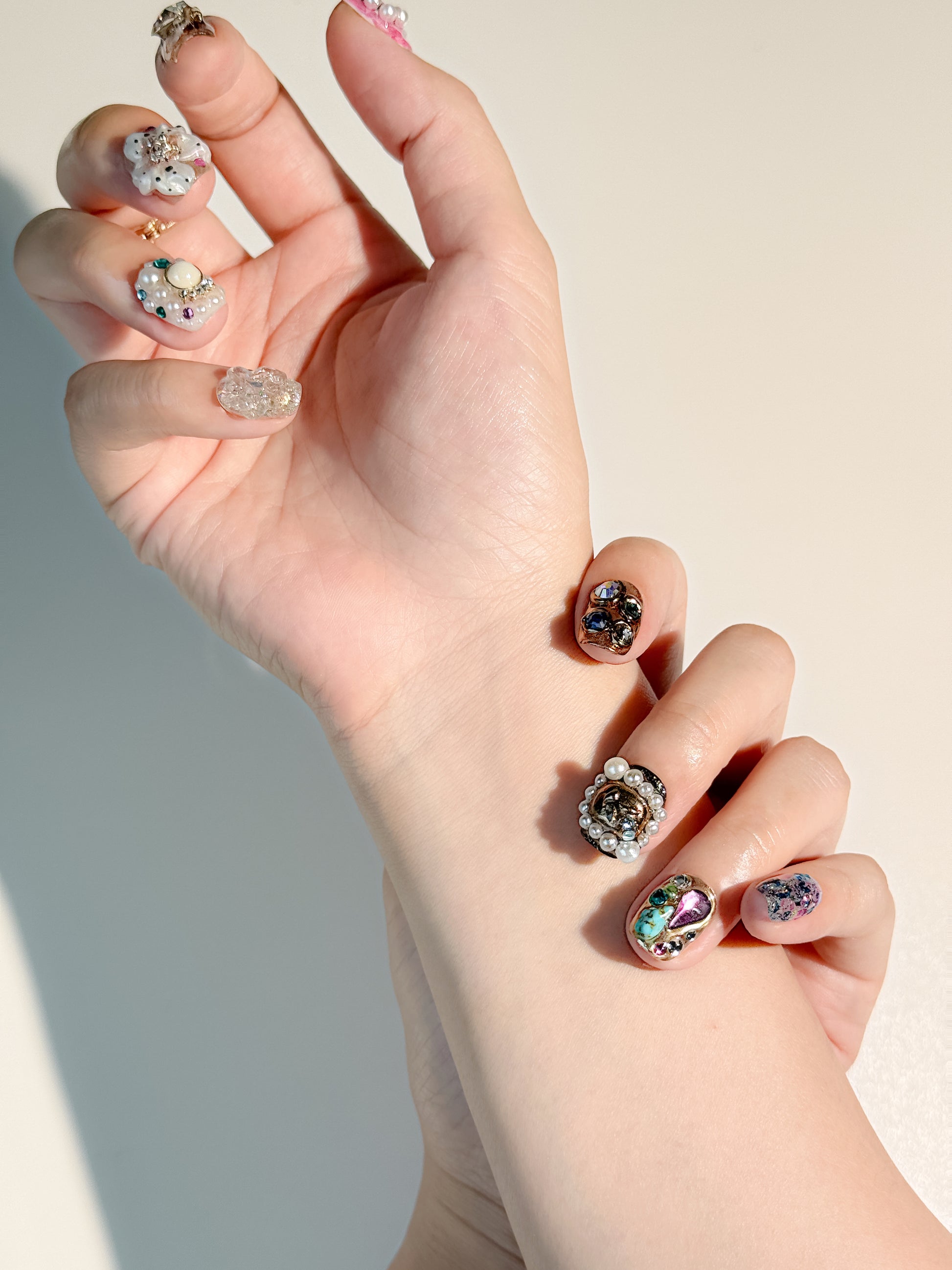 A full set of extravagant decoden-style 3D nails being worn, showcasing a mix of gold vintage elements, sparkling glitter, and oversized jewelry accents for a high-fashion manicure look.