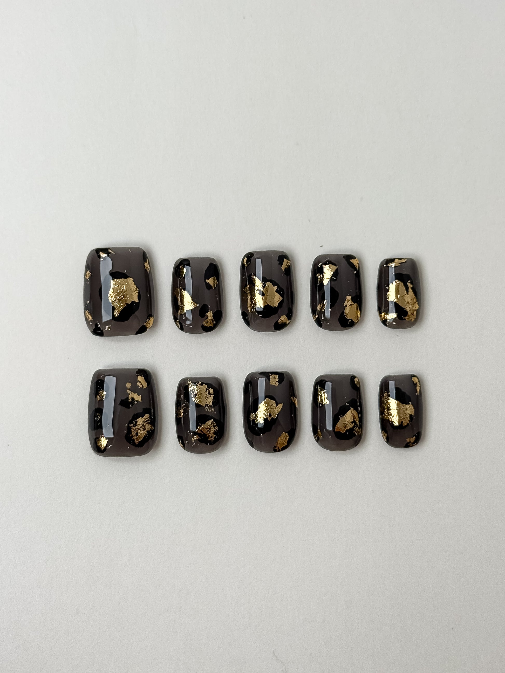 A 10-piece set of smoky grey leopard print press-on nails embellished with luxury gold foil flakes on a white background.
