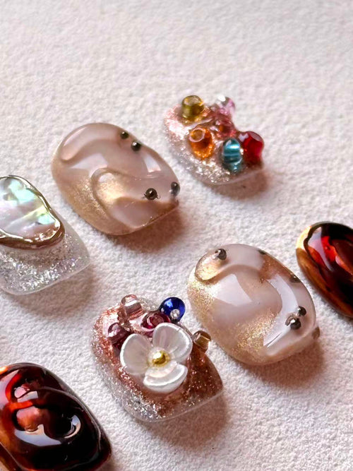 Close-up of 3D gel nail art showing intricate white flowers, gold glitter, and colorful gemstone accents.