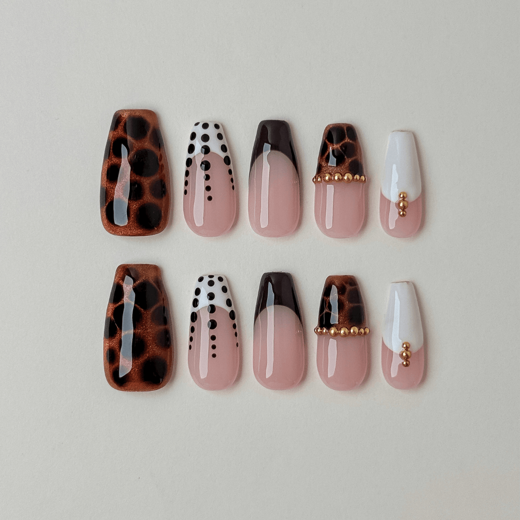 A set of ten false press-on nails in coffin shape arranged in two rows on a light beige background. The designs include leopard print, white with black dots, ombre, and white with gold bead accents.