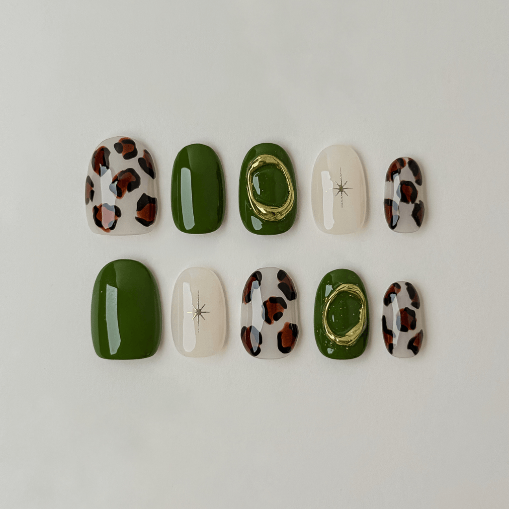 Ten press-on nails arranged in two rows on a plain light background. The set includes solid forest green, glossy white with a small star detail, leopard print with brown and black spots, and one green nail with a gold ring accent.