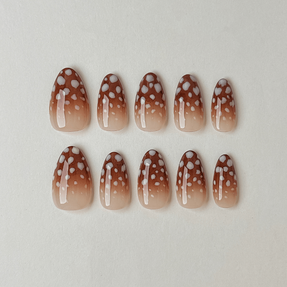 Handgemachte Press-On Nägel in Mandelform mit braunem Ombré-Farbverlauf und gepunktetem Rehkitz-Muster.