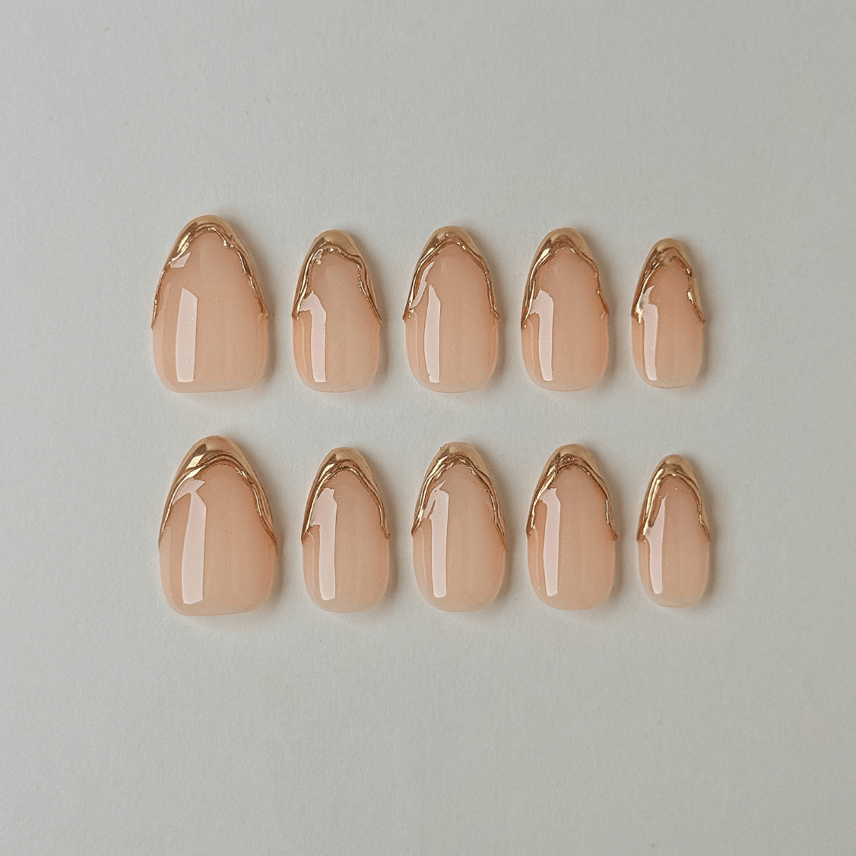 Handgemachte Press-On Nägel in Nude mit 3D Gold-Chrome French-Spitzen in geschwungener Mandelform.