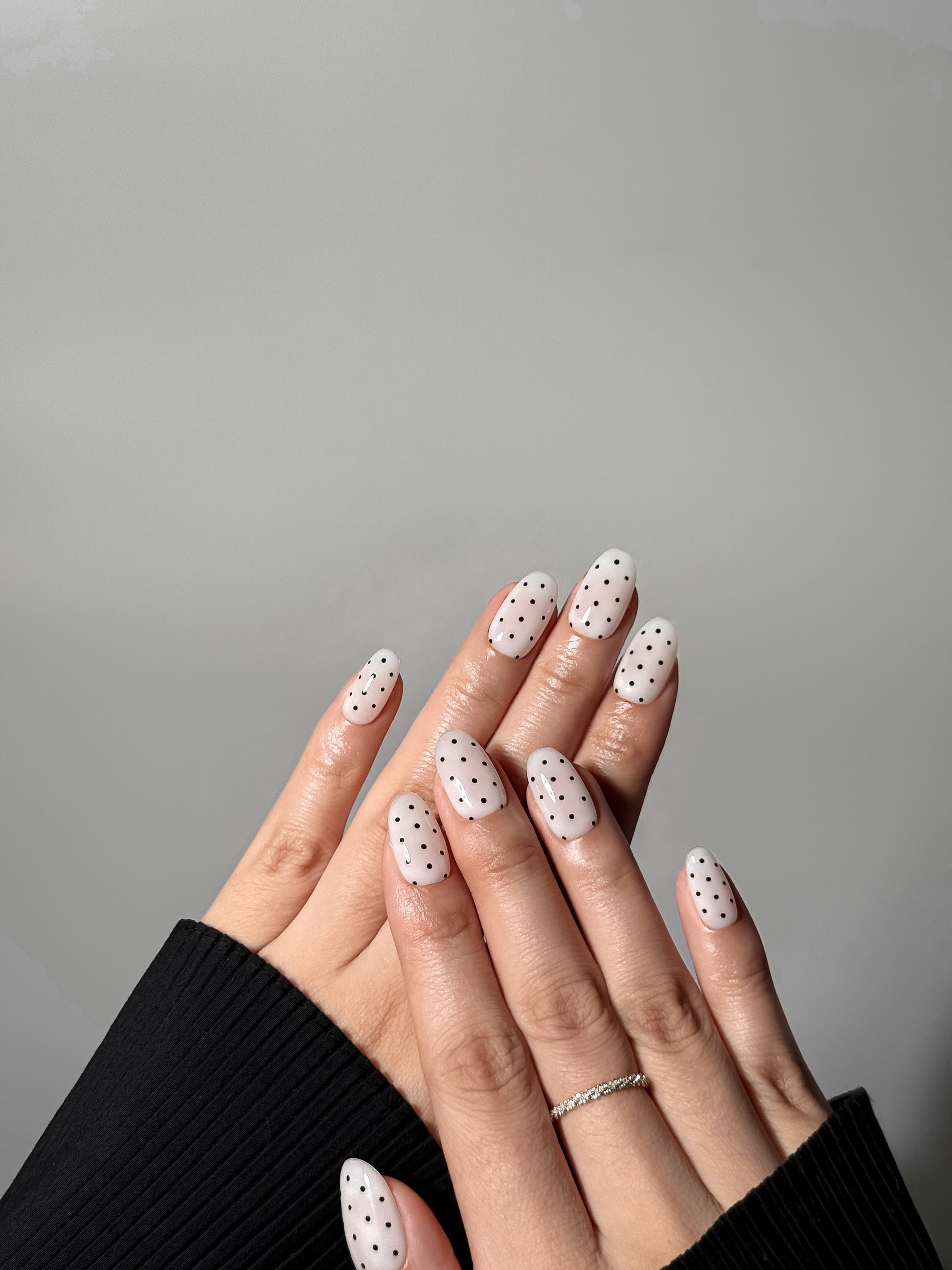 white with black dots press on nails that are in almond shape. on hand model