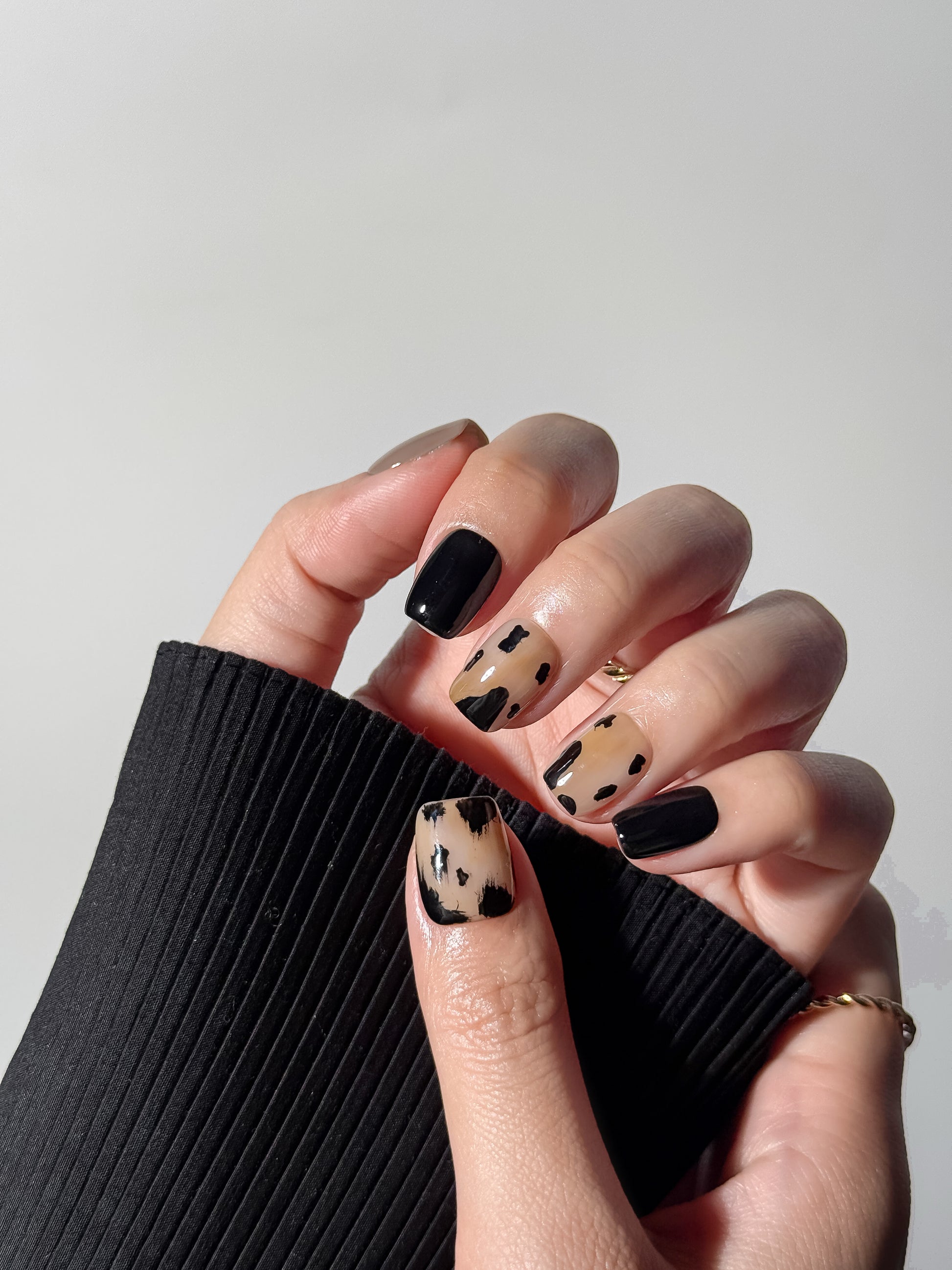 Hand wearing abstract black and tan cow print press-on nails paired with solid black and mocha brown accent nails.