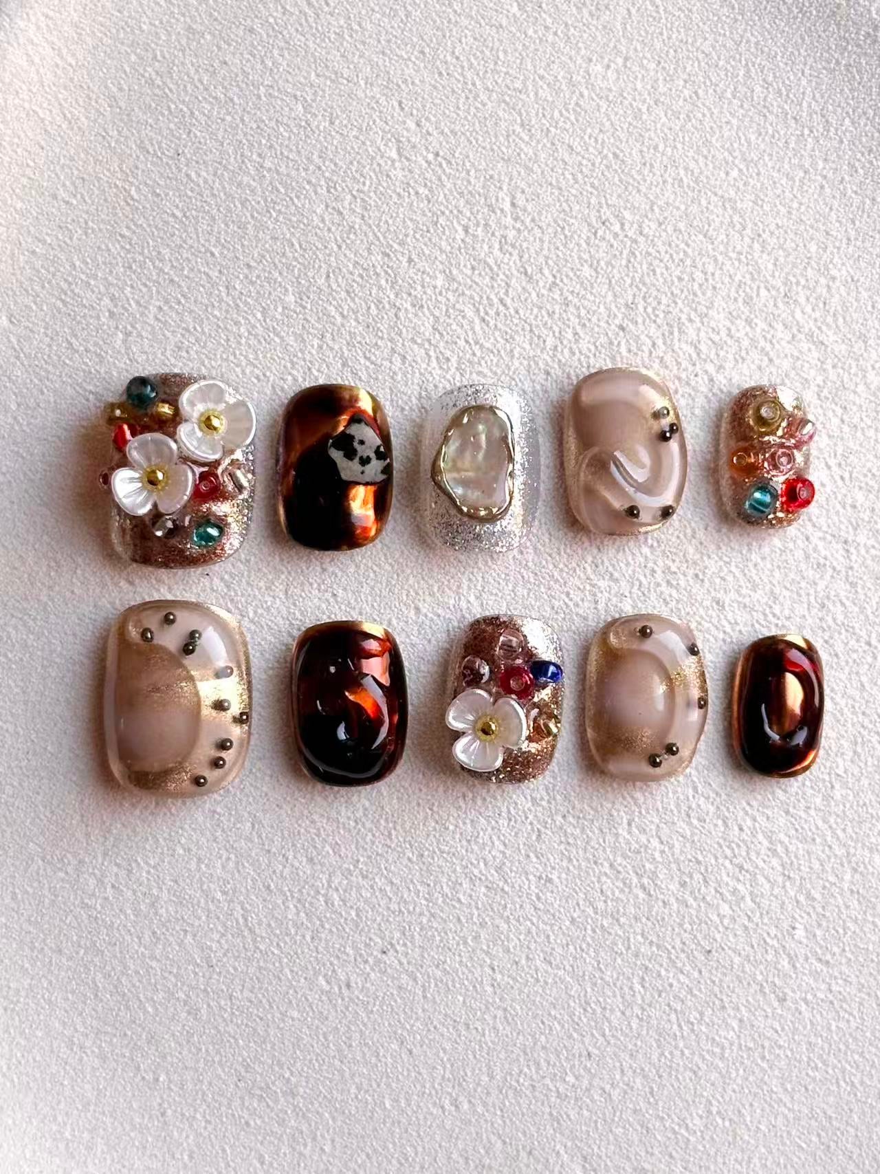 Overhead view of designer press-on nails with iridescent shell inlay and amber marble texture