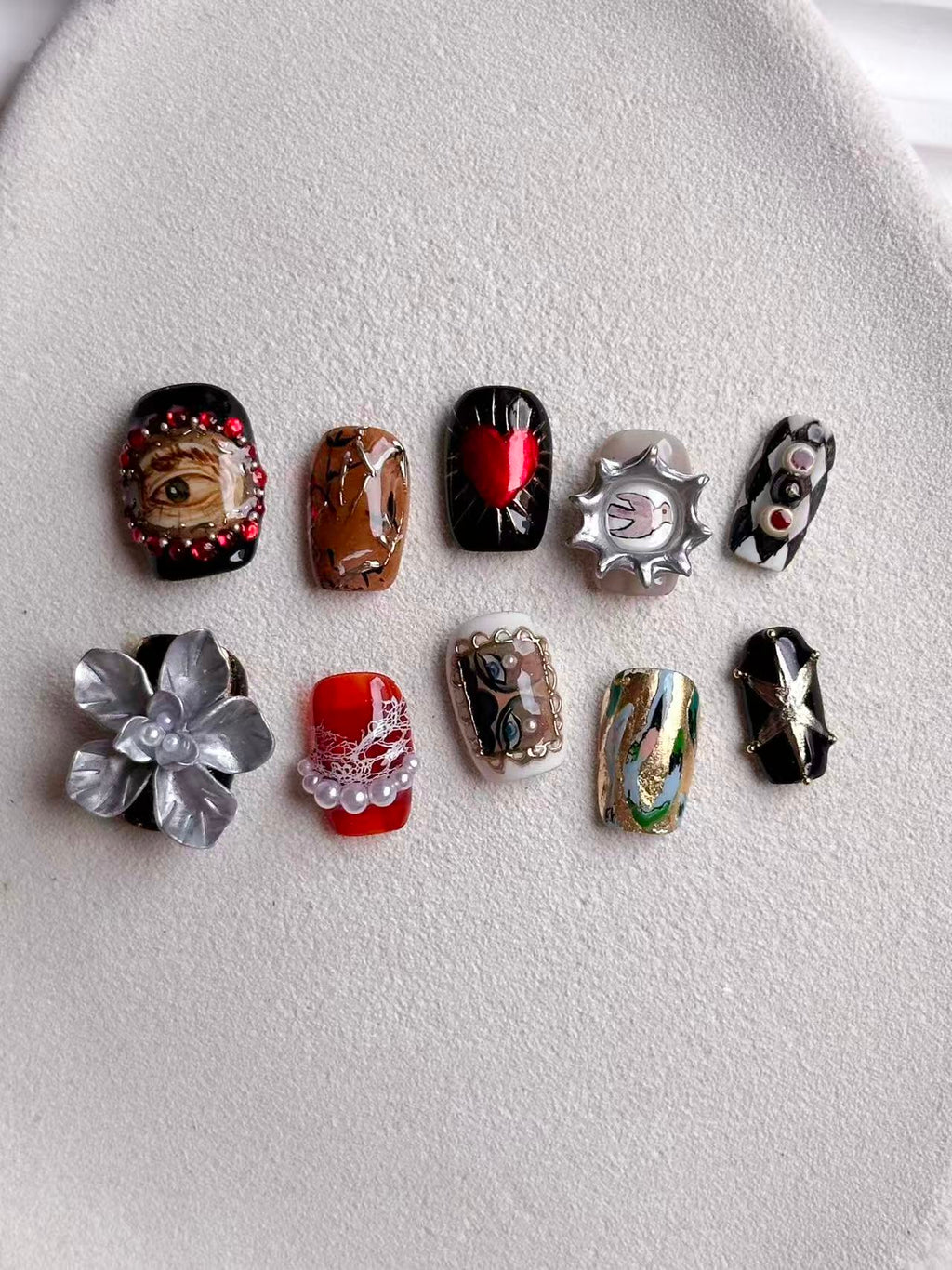 Flatlay of a 10-piece luxury nail set with eclectic surrealist designs and architectural 3D accents.