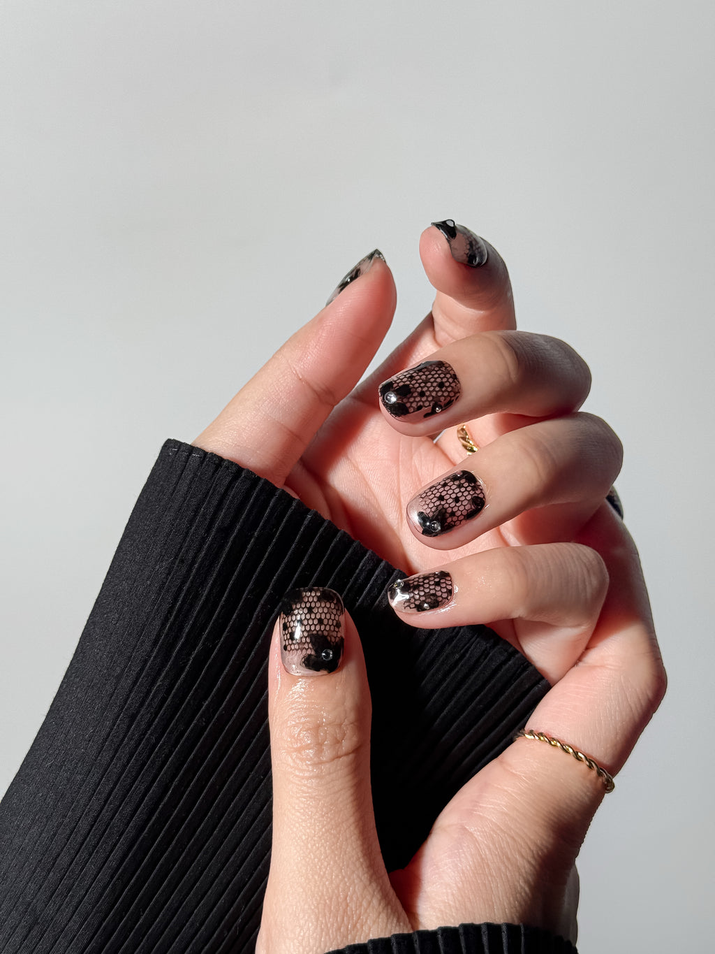 Close-up of a transparent lace manicure in short square shape, styled with a black ribbed sweater