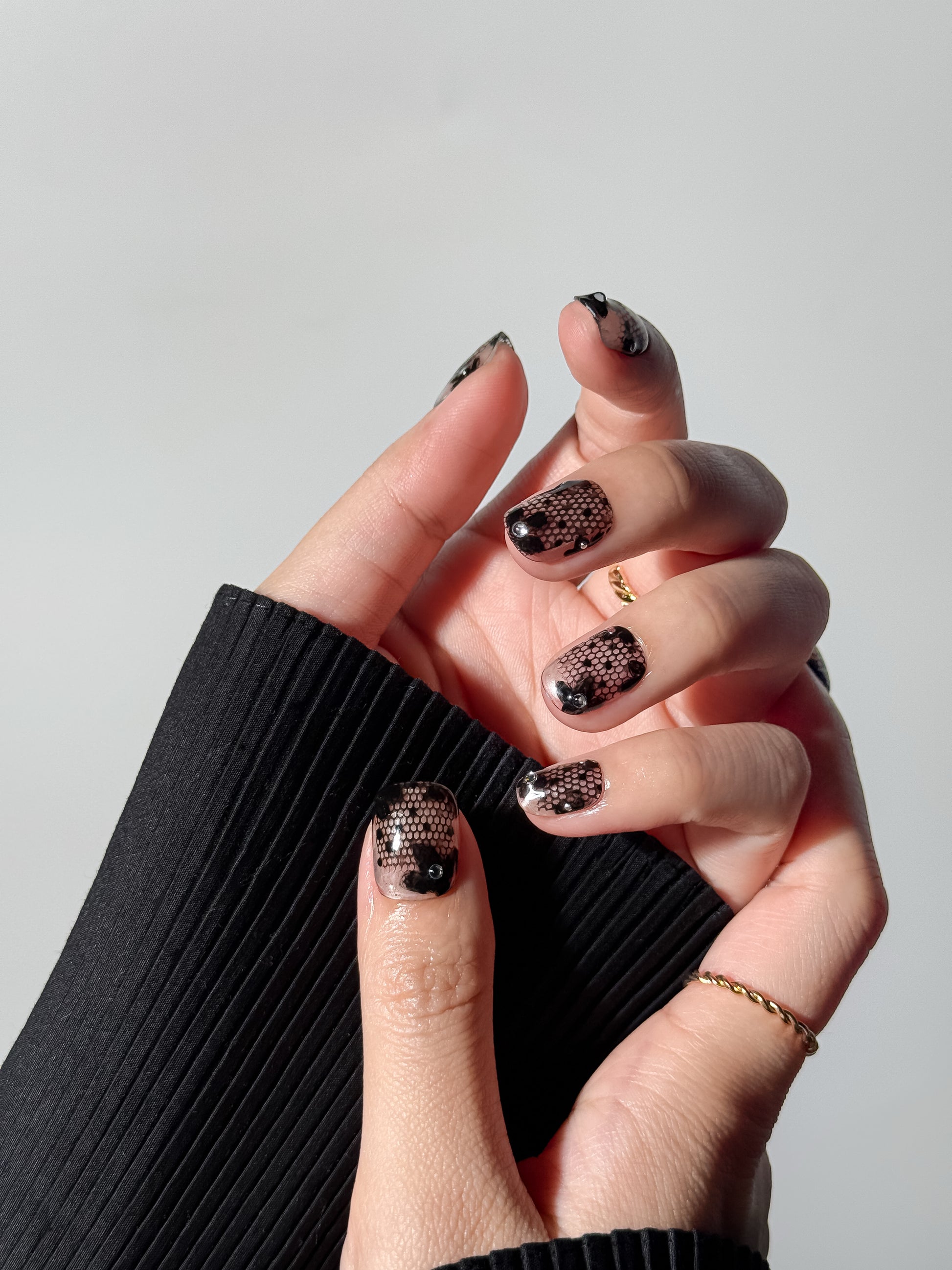 Close-up of a transparent lace manicure in short square shape, styled with a black ribbed sweater