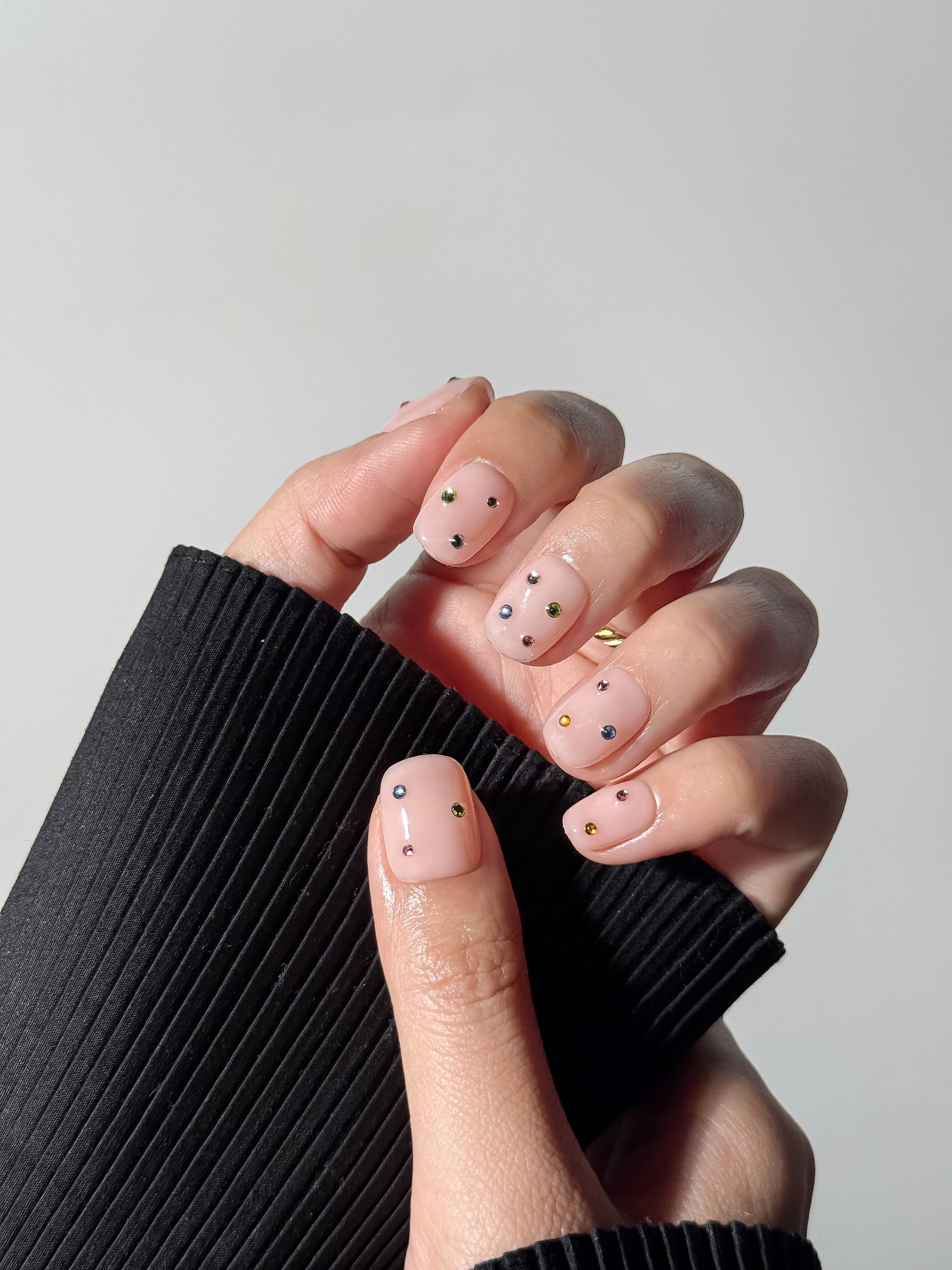 Model wearing Twinkle Pop nude press-on nails with multicolored crystals – reusable and easy to put on in 10 minutes