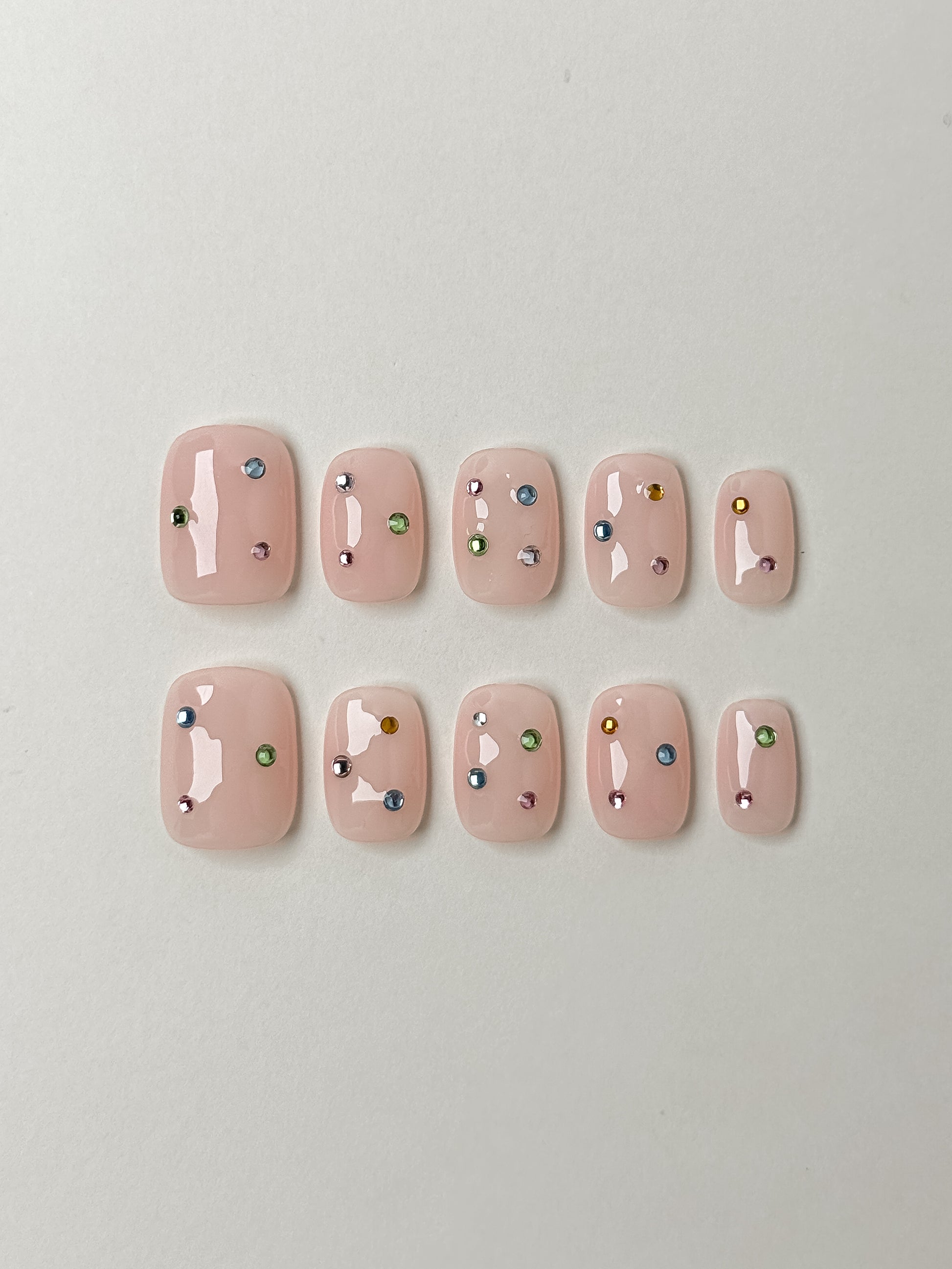 Flat lay of Twinkle Pop short square nude press-on nails with colorful gem accents – Justmee