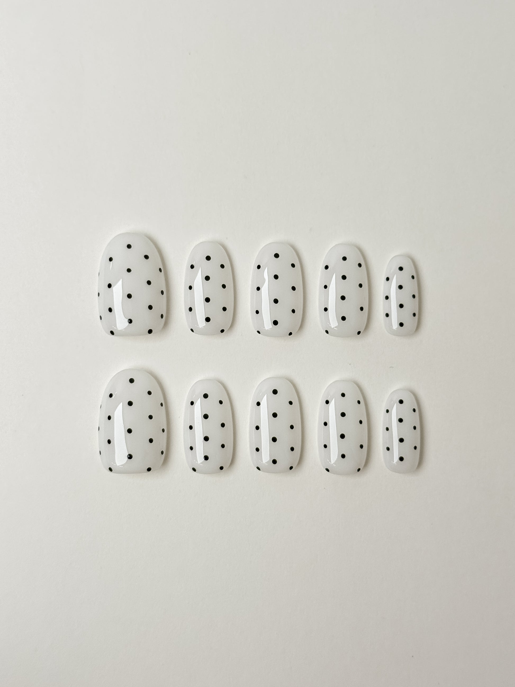 justmee press on nails in almond shape that are white with black dots. reusable and trendy styles